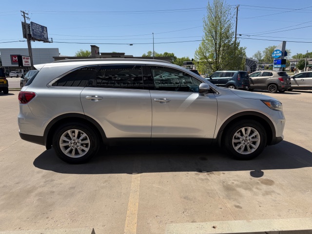 Side profile of a silver mid-size SUV parked in a sunny parking lot, with other cars in the background.