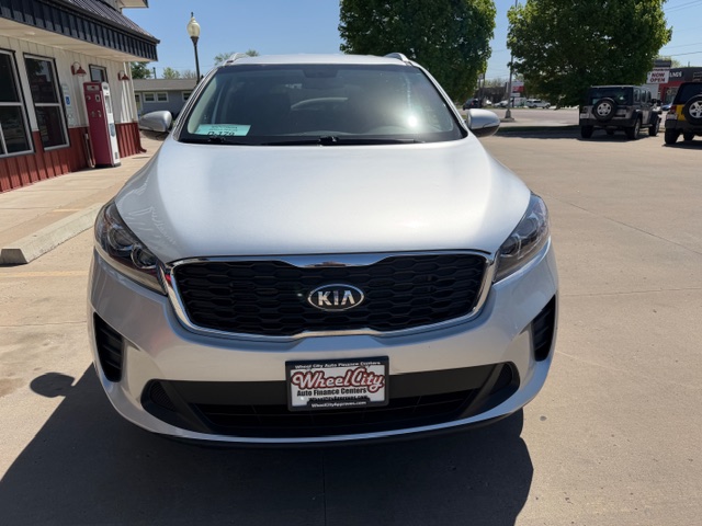 Front view of a white Kia SUV parked in a dealership lot, with a Wheel City Auto Finance Centers license plate frame.