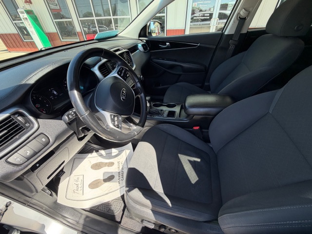 Driver's-seat interior of a black-cloth car with steering wheel, dashboard, and center console visible from the open door.