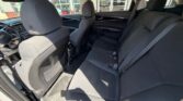 Dark fabric car interior with front seats visible and a three-seat back bench, sunlit through open doors, showing seat belts and floor mats.