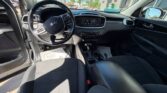 Inside a Kia car showing the steering wheel, dashboard, gear shifter, and front seats, with sunlight through the windows.
