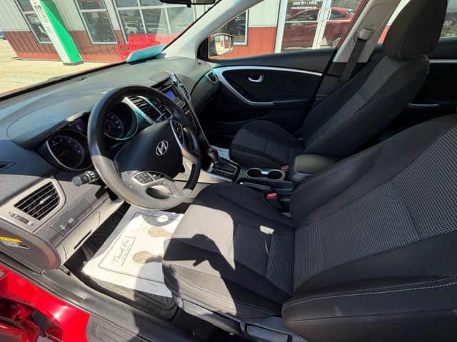 Front interior of a black Hyundai sedan, showing the driver’s seat and steering wheel, center console, and front passenger seat as seen from the open driver's side door.