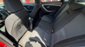 Back seat area of a red car with black fabric upholstery: two outer passenger seats and a middle seat, front seat visible, door panels, and floor mats illuminated by daylight.