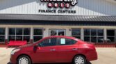Red four-door sedan parked in front of the Wheel City Auto Finance Centers storefront under a clear blue sky.