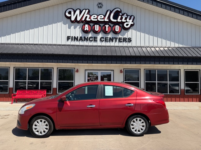 Red four-door sedan parked in front of the Wheel City Auto Finance Centers storefront under a clear blue sky.
