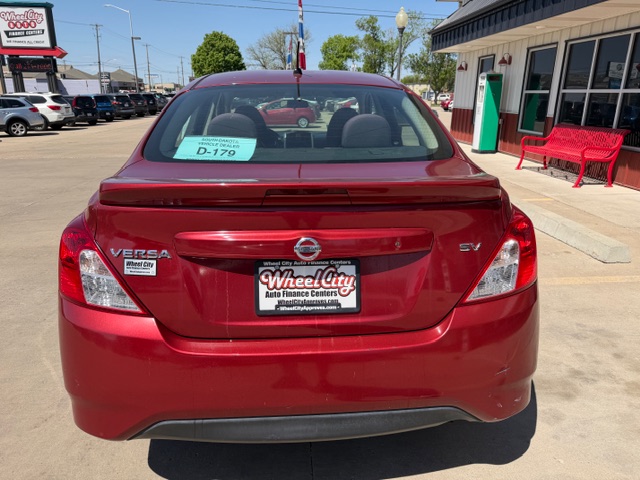 Rear view of a red Nissan Versa SV parked in a dealership lot; window sticker and Wheel City Auto Finance Centers plate frame are visible.
