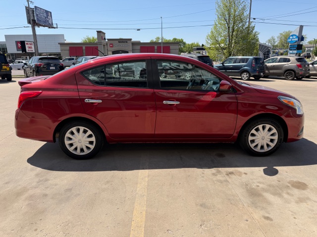 Side view of a red four-door sedan parked in a sunny dealership lot with other cars in the background, visible parking lines.