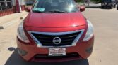 Front view of a red Nissan SUV parked in a dealership lot, with a Wheel City license plate holder on the bumper and a dealership building in the background