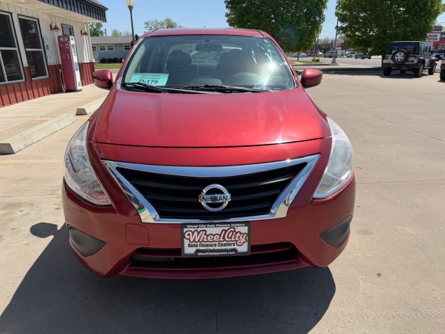 Front view of a red Nissan SUV parked in a dealership lot, with a Wheel City license plate holder on the bumper and a dealership building in the background