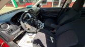 Front interior of a red car with black cloth seats, steering wheel on the left, center console and gear shifter visible, dashboard details illuminated by sunlight.