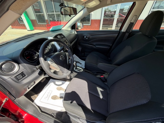 Front interior of a red car with black cloth seats, steering wheel on the left, center console and gear shifter visible, dashboard details illuminated by sunlight.