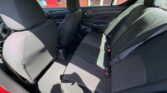 Interior of a red car showing the back seat with black fabric upholstery, three-seat bench, and visible seat belts; front seats and door panels are also in view.