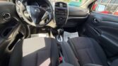 Interior of a Nissan car viewed from the back seat, showing the steering wheel, center console with radio and climate controls, automatic gear shifter, and black cloth front seats with sunlight streaming through the windows.