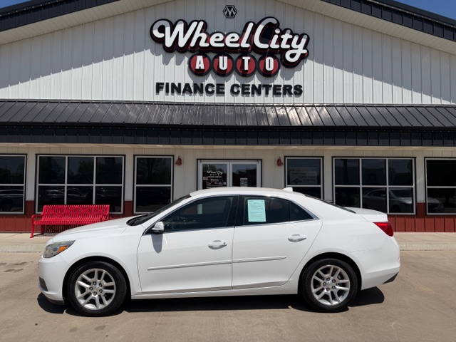White sedan parked in front of Wheel City Auto Finance Centers dealership building.