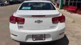 Rear view of a white Chevrolet sedan parked in a dealership lot with a Wheel City license plate frame and a dealership tag on the rear window