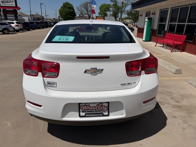 Rear view of a white Chevrolet sedan parked in a dealership lot with a Wheel City license plate frame and a dealership tag on the rear window