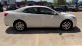 White four-door sedan photographed from the side in a parking lot, with other vehicles and storefronts in the background.