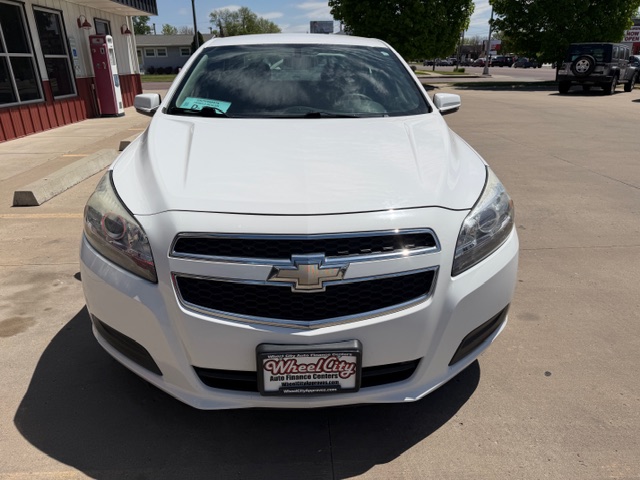 Front view of a white Chevrolet sedan parked in a dealership lot, license plate reads Wheel City Auto Finance Centers.