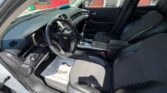 Interior of a white Chevrolet sedan: driver’s seat, front passenger seat, steering wheel with Chevy logo, dashboard, and center console; driver's door is open.