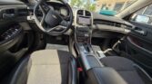 Front interior of a Chevrolet car showing steering wheel, center touchscreen console, gear shifter, and black cloth seats with daylight coming through the windows.