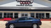 Blue two-door sedan parked in front of the Wheel City Auto Finance Centers storefront, with a red bench visible to the left.