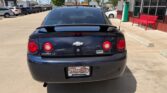 Rear view of a dark blue Chevrolet Cobalt LT parked in a sunny car lot, dealership building visible to the right.
