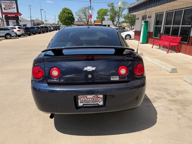 Rear view of a dark blue Chevrolet Cobalt LT parked in a sunny car lot, dealership building visible to the right.