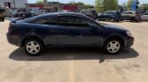 Side view of a dark blue two-door coupe parked in a parking lot, with other cars and a row of buildings in the background.