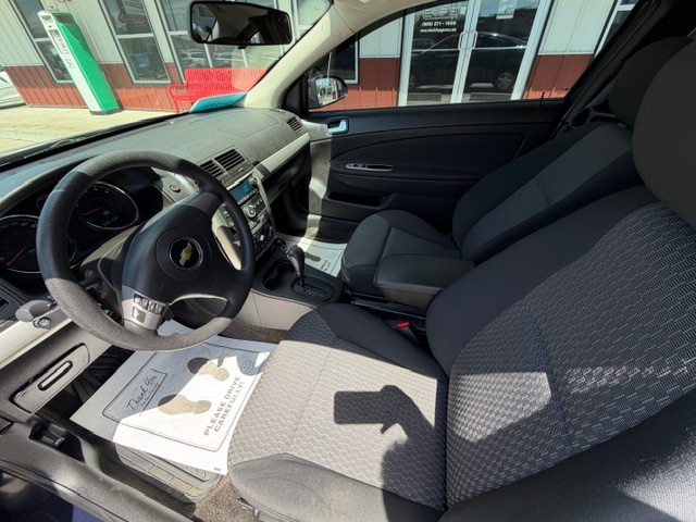 Interior of a Chevrolet car showing the driver and front passenger seats, steering wheel, center console, and dashboard.