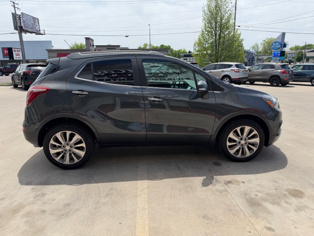 Side view of a dark gray compact SUV in a dealership lot, four doors, alloy wheels, and roof rails.