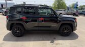 Side view of a black Jeep Renegade with red door handles parked in a car dealership lot, with other cars in the background.