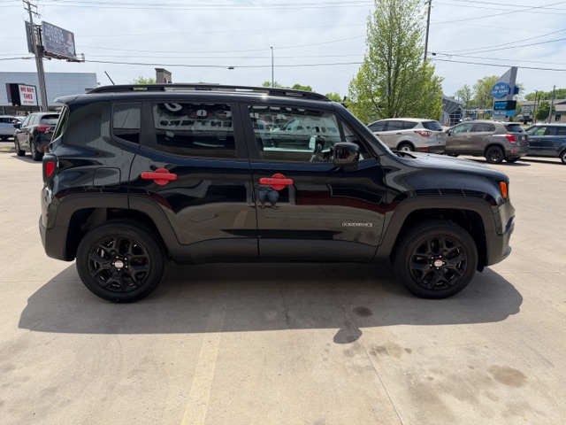Side view of a black Jeep Renegade with red door handles parked in a car dealership lot, with other cars in the background.