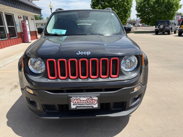 Front view of a dark gray Jeep SUV with red accented grille, parked in a lot outside a storefront; dealer plate reads Wheel City Auto Finance Centers.