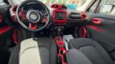Front interior of a black Jeep with bold red trim: steering wheel, center touchscreen, climate controls, gear selector, and red accents on air vents and door panels.