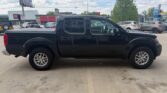 Black crew-cab pickup truck parked in a dealership lot, shown in a clear side profile with a long cargo bed and alloy wheels.