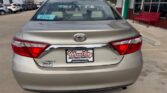 Rear view of a beige Toyota Camry LE parked at a Wheel City Auto Finance Centers lot, with a dealership plate frame on the bumper.