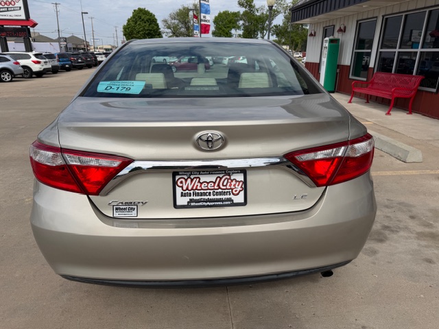 Rear view of a beige Toyota Camry LE parked at a Wheel City Auto Finance Centers lot, with a dealership plate frame on the bumper.