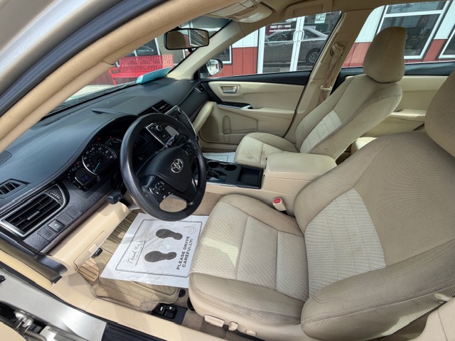 Interior of a beige sedan showing the driver and front passenger seats, dashboard, steering wheel, and center console with a floor mat on the driver’s side.