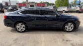 Side view of a dark blue Chevrolet Impala sedan parked in a parking lot, with tinted windows and alloy wheels, storefronts in the background.