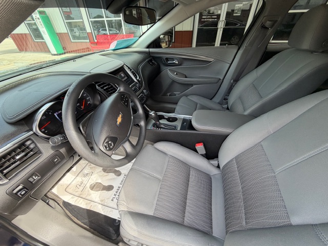 Front interior of a Chevrolet car showing gray cloth seats, steering wheel with Chevrolet emblem, center console, and dashboard view