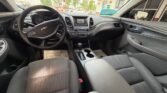 Front interior of a Chevrolet: steering wheel with logo, center console, and black cloth seats visible from the driver’s seat view at a dealership.