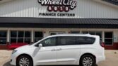 White minivan parked in front of a Wheel City Auto Finance Centers storefront on a sunny day, with glass doors and red benches by the entrance