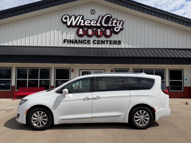 White minivan parked in front of a Wheel City Auto Finance Centers storefront on a sunny day, with glass doors and red benches by the entrance