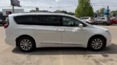 Side view of a white minivan parked in a parking lot, with tinted windows and sliding doors along the side.