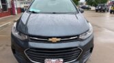 Front view of a dark gray Chevrolet SUV with raindrops on the hood, parked in a dealership lot near a red building; license plate frame reads Wheel City Auto Finance Centers.