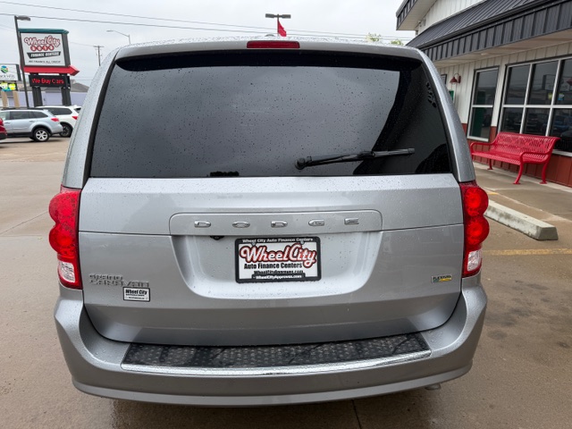 Rear view of a silver Dodge minivan with a Wheel City dealer plate, parked in a dealership lot under a cloudy sky.