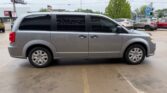Side view of a light gray minivan parked in a parking lot, with tinted windows and a sliding door visible on the passenger side.