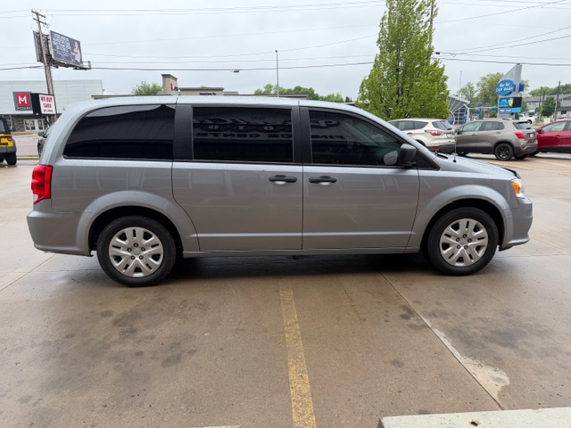 Side view of a light gray minivan parked in a parking lot, with tinted windows and a sliding door visible on the passenger side.
