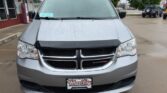 Front view of a silver Dodge minivan parked in a wet lot on a rainy day, featuring a black hood deflector and a Wheel City Auto Finance Centers license plate frame.