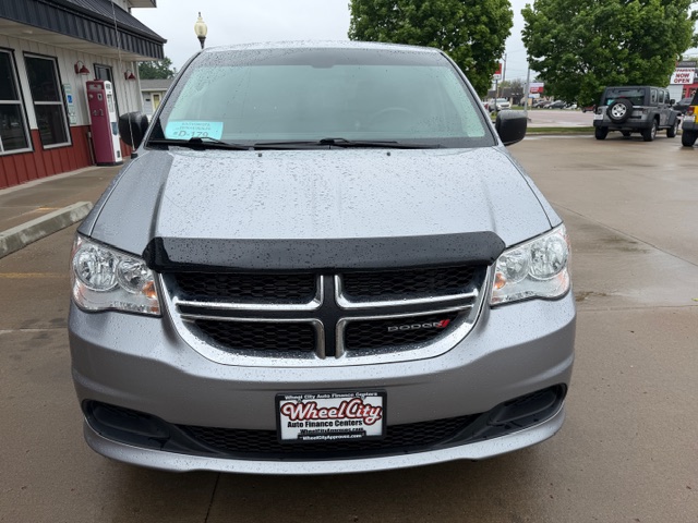 Front view of a silver Dodge minivan parked in a wet lot on a rainy day, featuring a black hood deflector and a Wheel City Auto Finance Centers license plate frame.